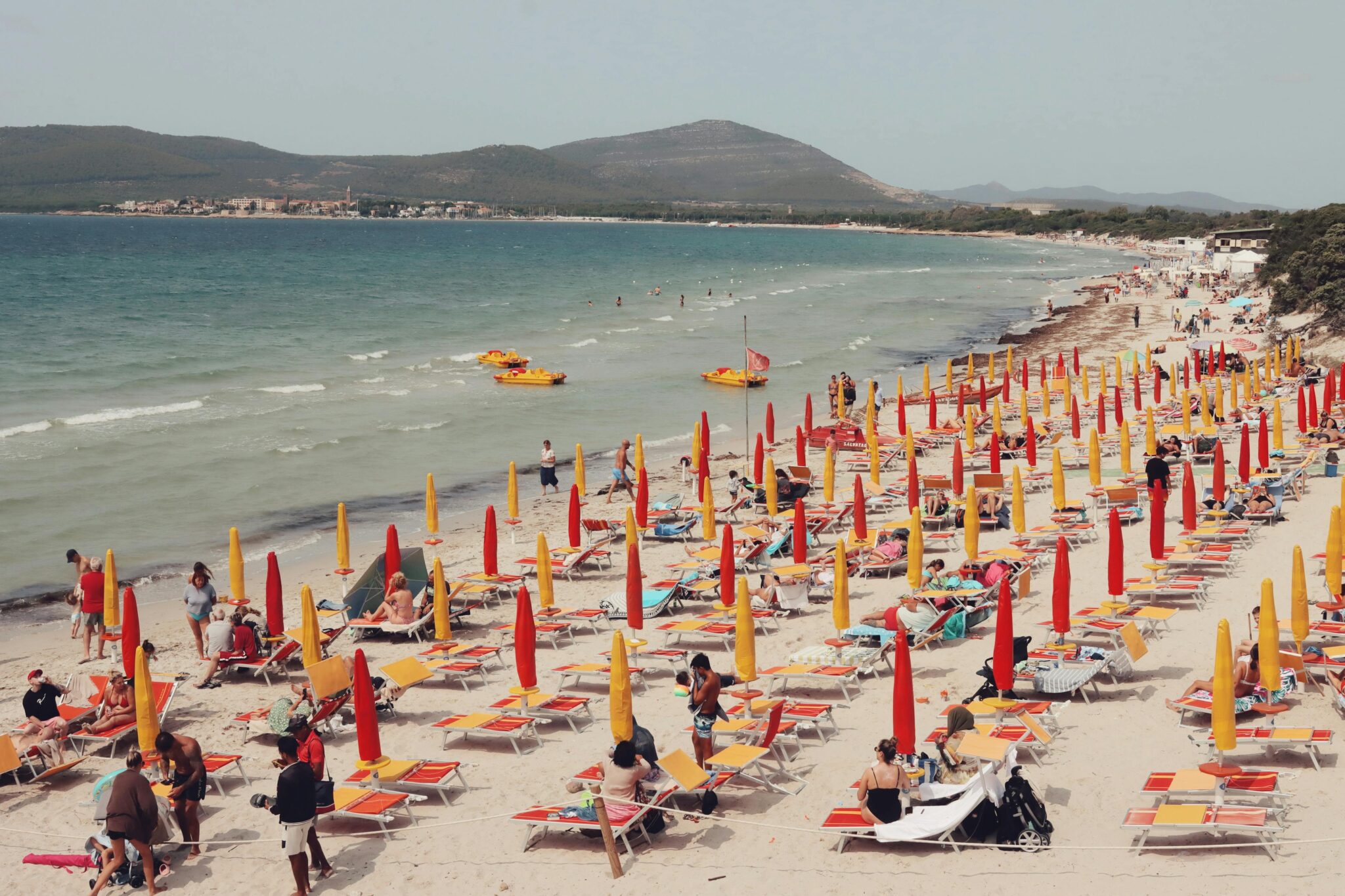 An inviting beach in Alghero, Sardinia, filled with vibrant umbrellas and sunbathers.