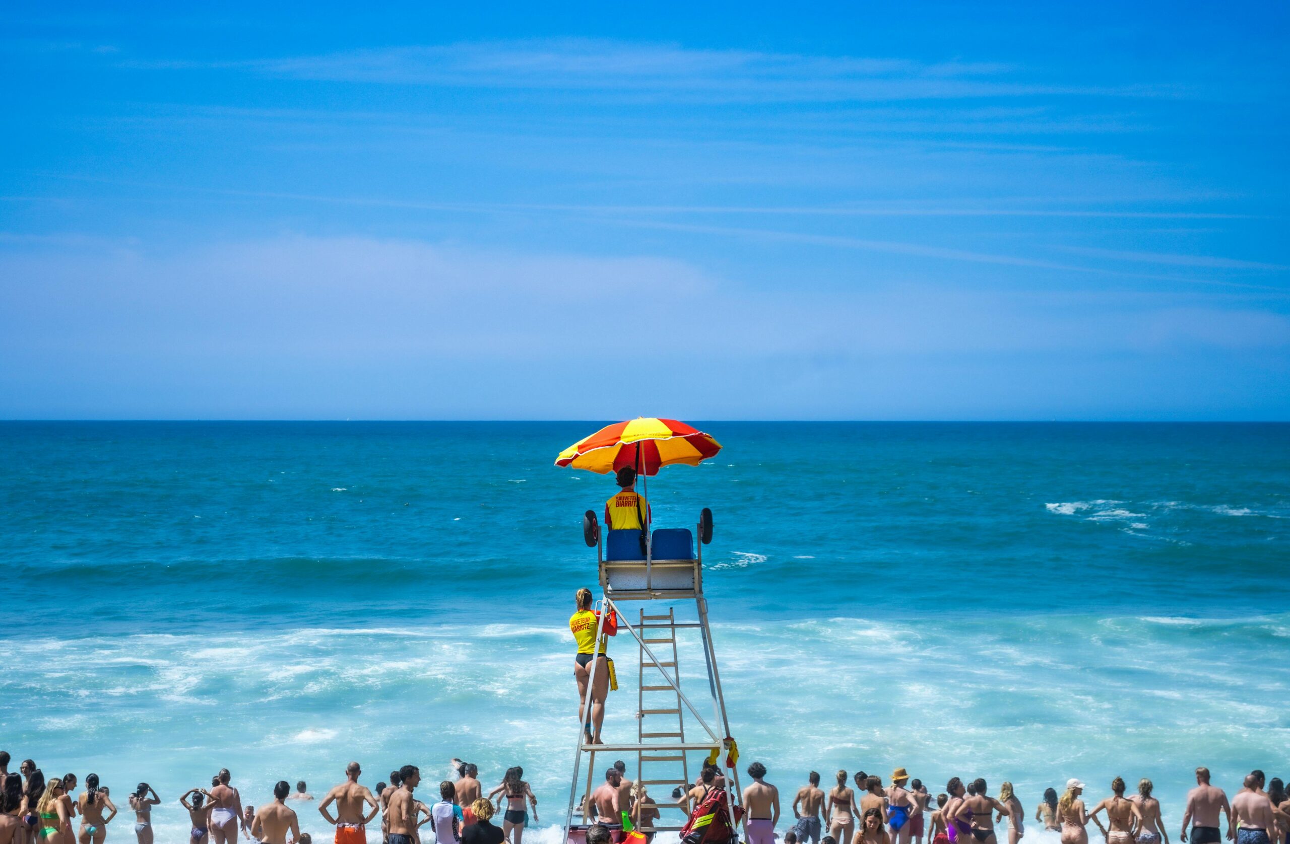 Lifeguard overlooking a crowded beach under a colorful umbrella, capturing a vivid summer day.