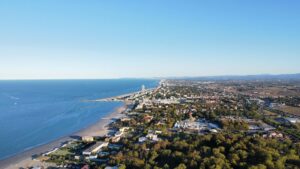 Sun-drenched aerial view of a coastal city with a vast blue ocean and sandy beachline, showcasing summer vibes.