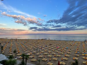 A serene beach scene with rows of empty chairs under a colorful sunset sky.