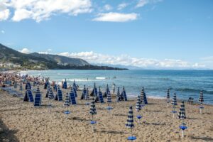 A scenic beach in Sicily, Italy, with rows of umbrellas and people enjoying the sun and sea.