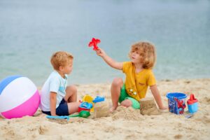 Two kids enjoy playing with toys on a sunny beach day, building sandcastles together.