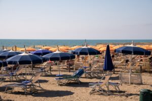 Sunny beach scene in Italy with colorful sun umbrellas and lounge chairs, perfect for summer relaxation.
