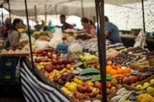 Colorful variety of fresh fruits at an outdoor market with shoppers in view.