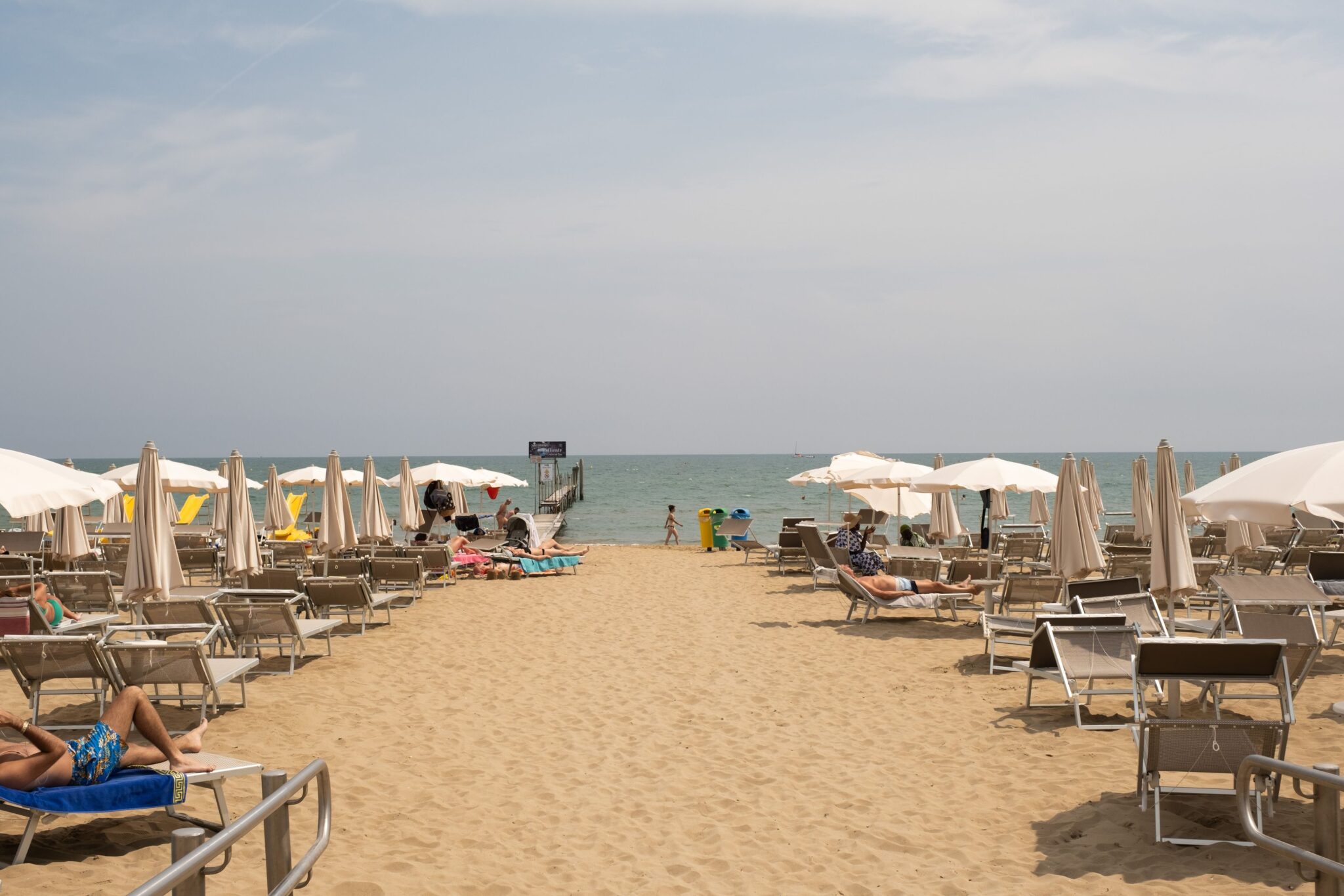 Tourists enjoying a sunny day at Lido di Jesolo beach in Veneto, Italy, with sun loungers and umbrellas.