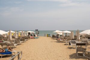 Tourists enjoying a sunny day at Lido di Jesolo beach in Veneto, Italy, with sun loungers and umbrellas.