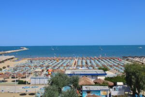 Aerial view of crowded Ortona beach with umbrellas and boats on a sunny summer day.