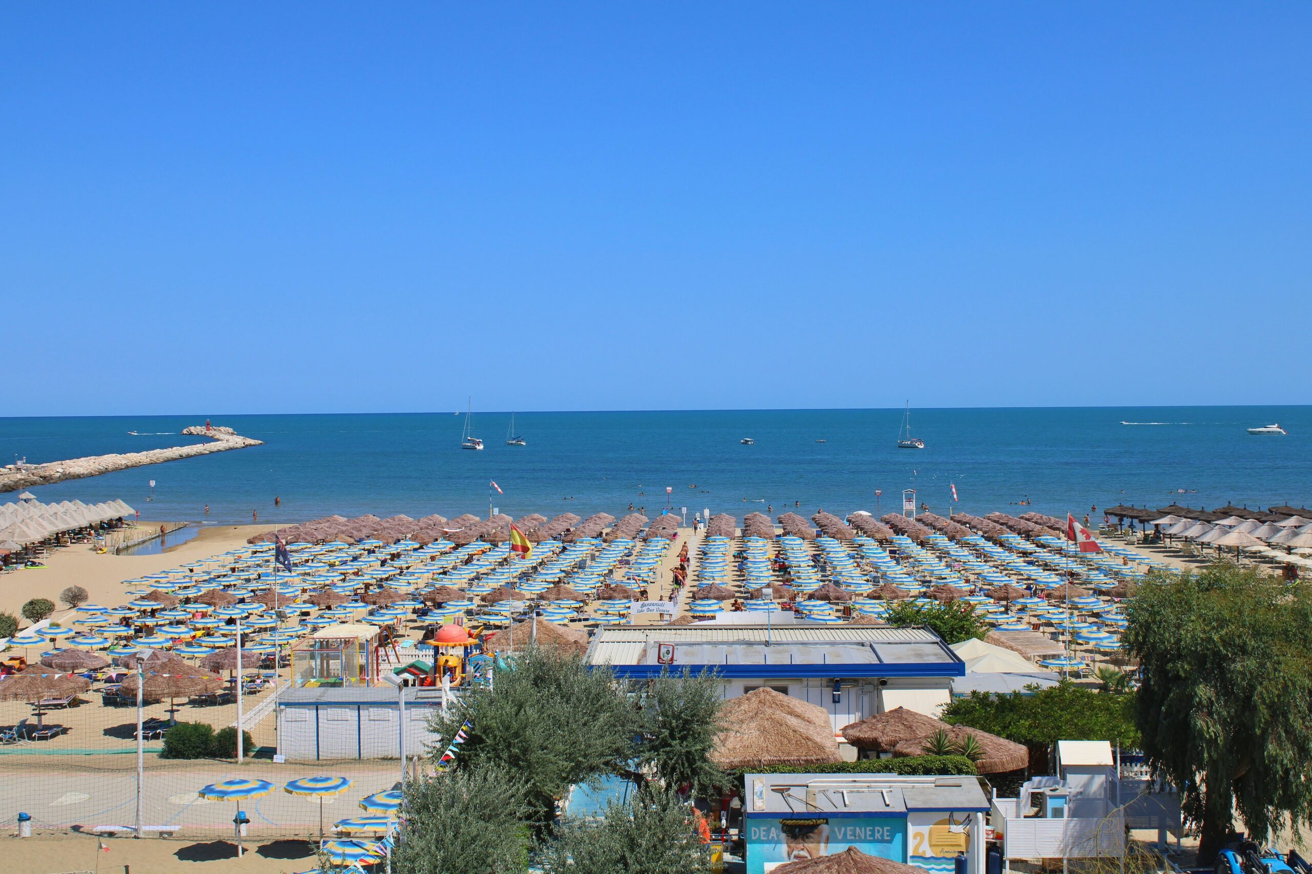Aerial view of crowded Ortona beach with umbrellas and boats on a sunny summer day.