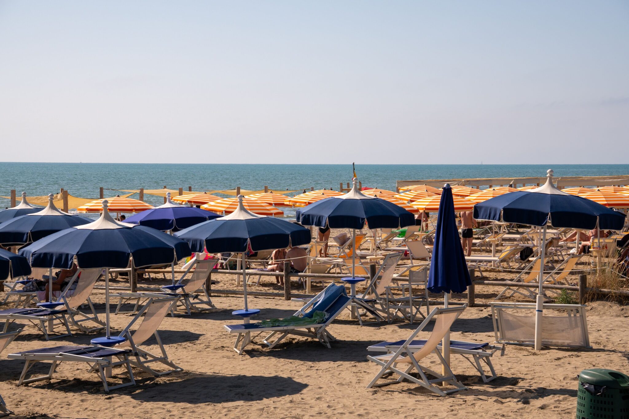 Sunny beach scene in Italy with colorful sun umbrellas and lounge chairs, perfect for summer relaxation.